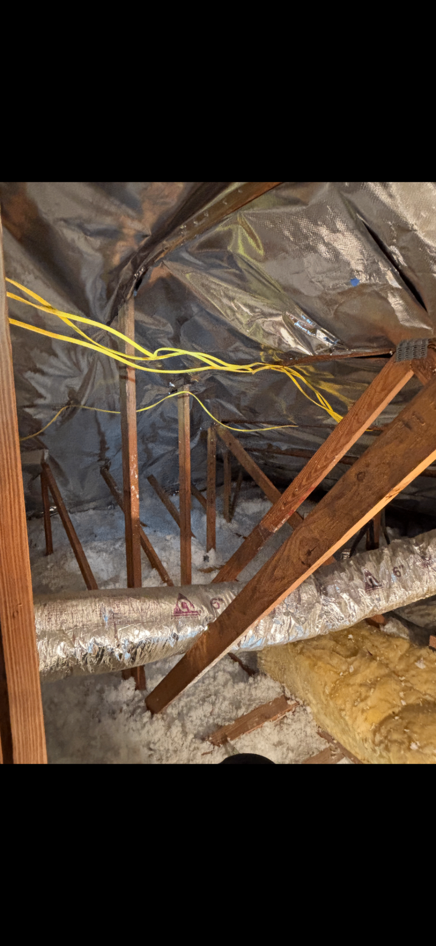 Radiant barrier foil covering attic rafters with electrical wiring visible
